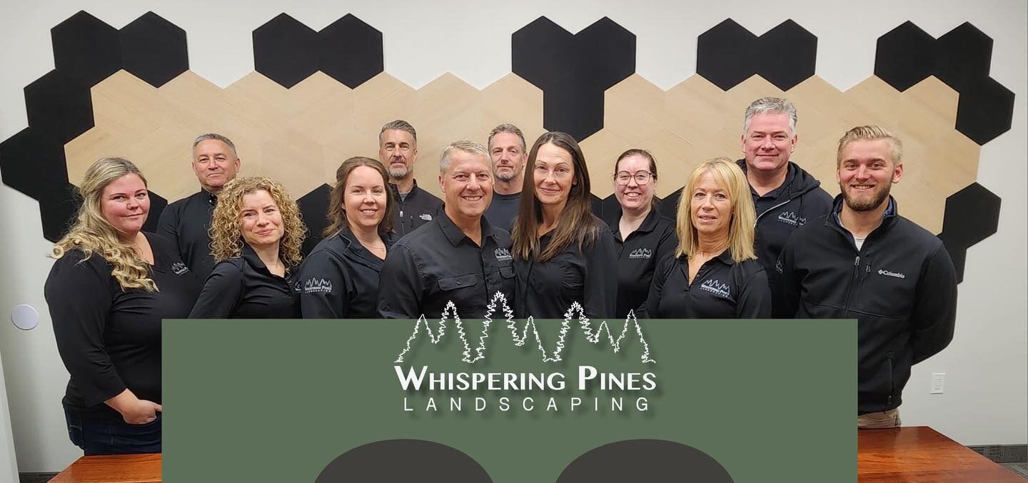 A group of people from Whispering Pines Landscaping celebrate their 30th anniversary, standing indoors with a decorated wall behind them.