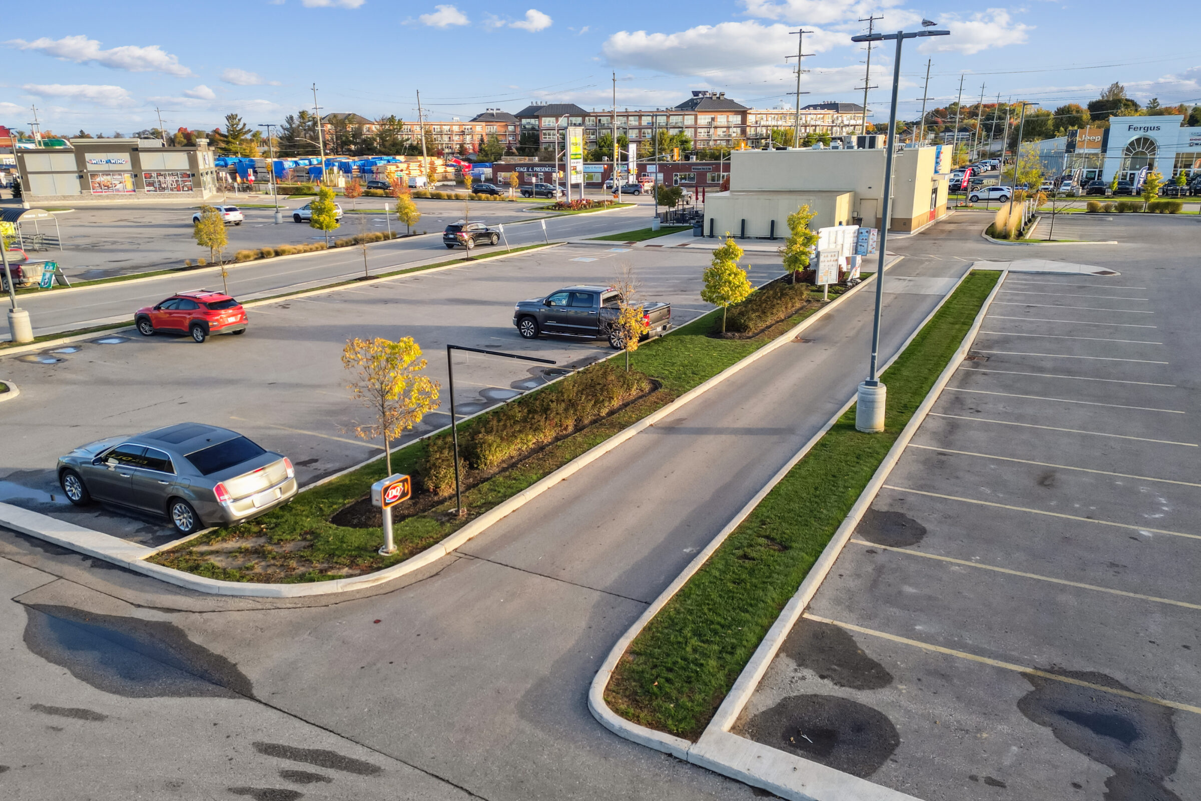 Aerial view of a mostly empty parking lot with a Dairy Queen sign, surrounded by buildings and cars, under a partly cloudy sky.
