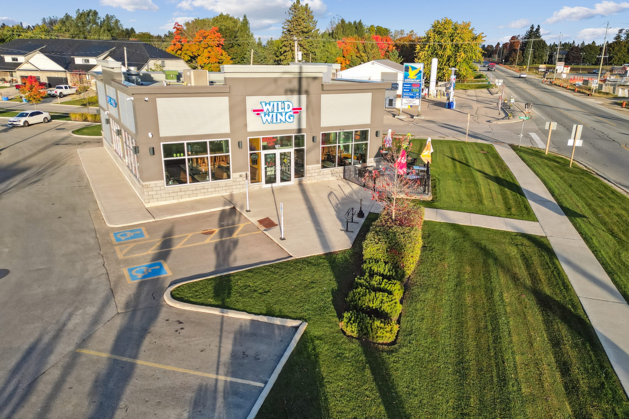 A restaurant building with a "Wild Wing" sign, parking spaces, green lawn, and a road intersecting at the corner in a suburban area.