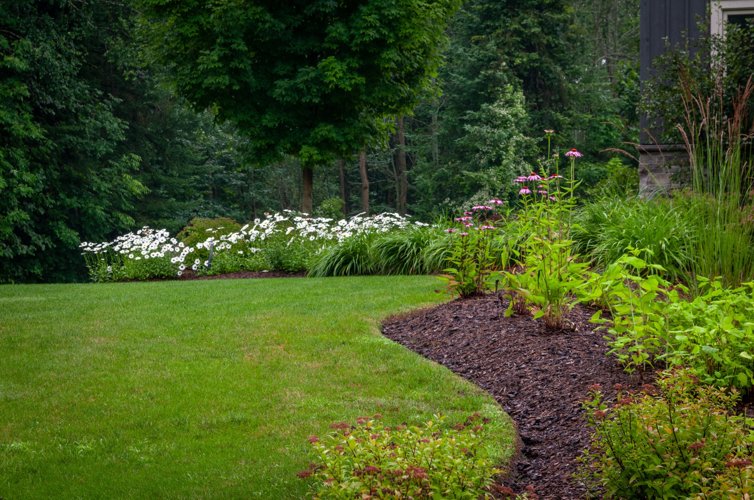 A lush garden with vibrant greenery, blooming flowers, and trees. The well-manicured lawn and flower beds create a serene, picturesque scene.