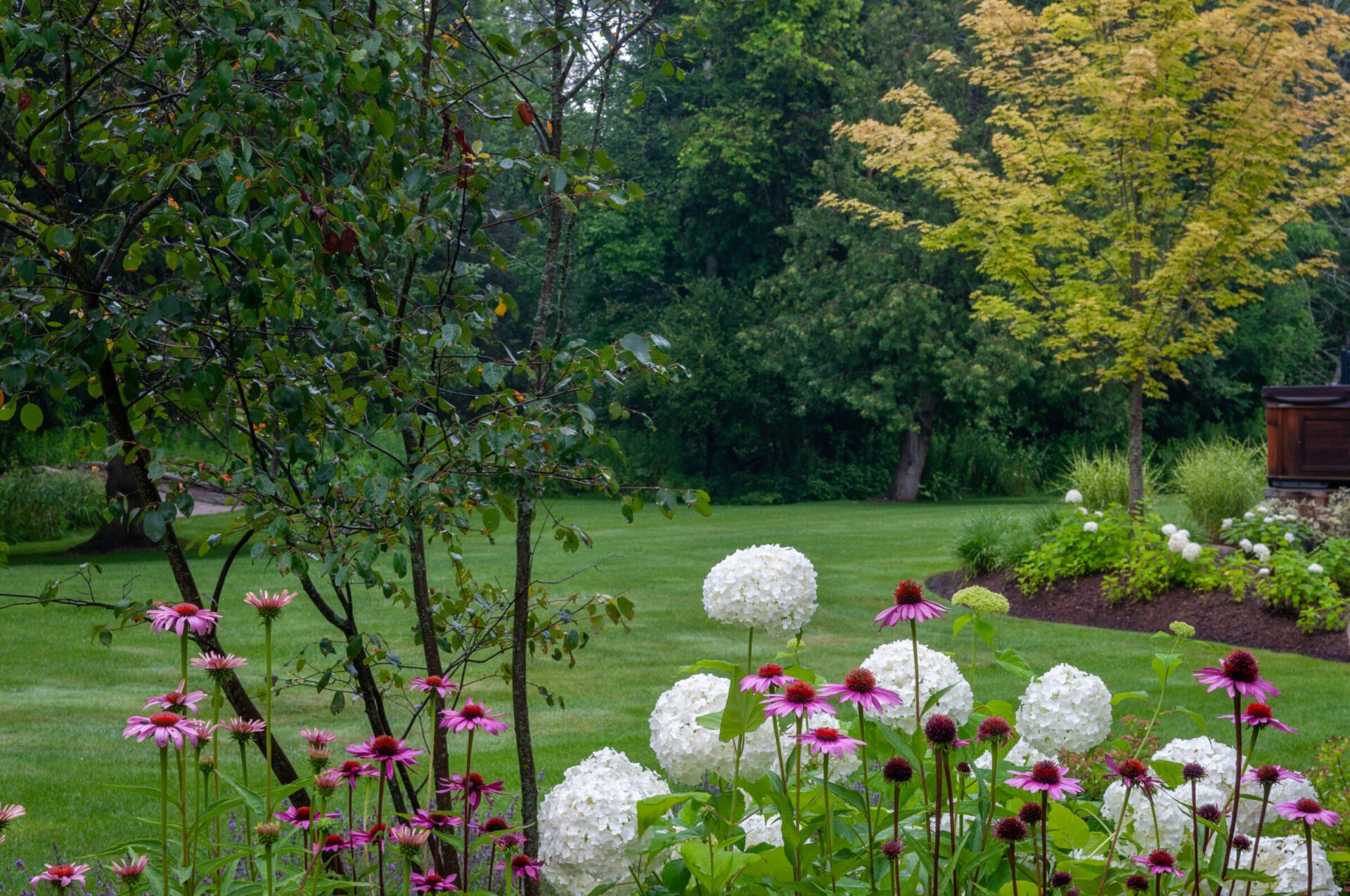 A lush garden with vibrant pink and white flowers, surrounded by green trees and a maintained lawn, evokes serenity.