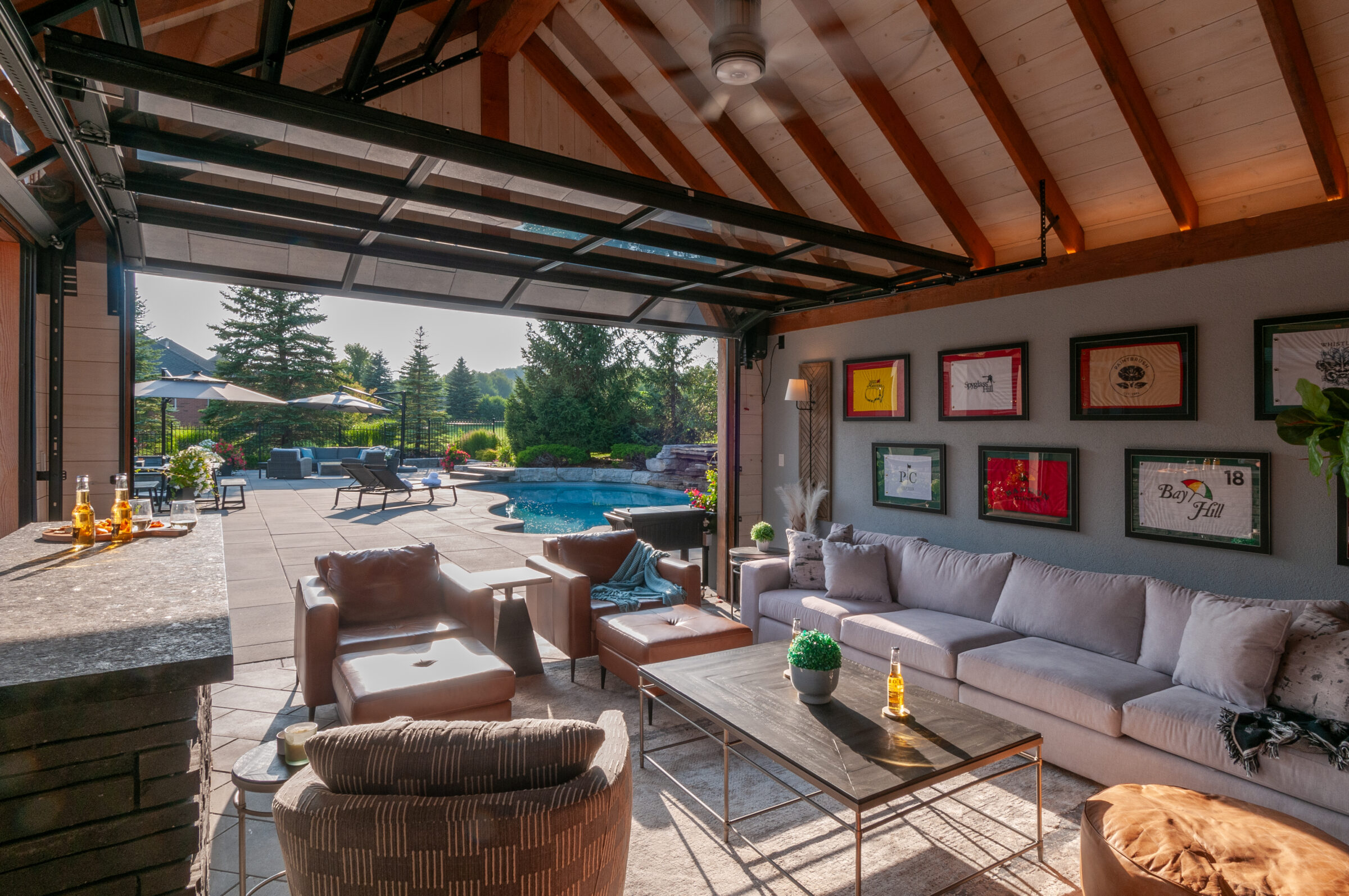Luxurious outdoor living space with cozy seating, framed golf flags, and a view of a pool and landscaped garden on a sunny day.