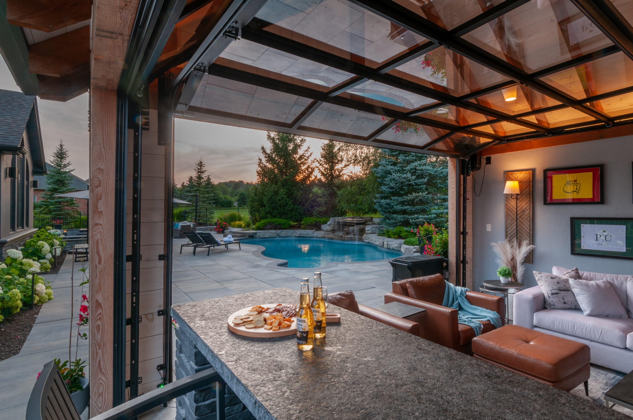 Modern patio with pool view, cozy seating area, and snacks on the counter. Surrounded by trees and garden, creating a serene ambiance.