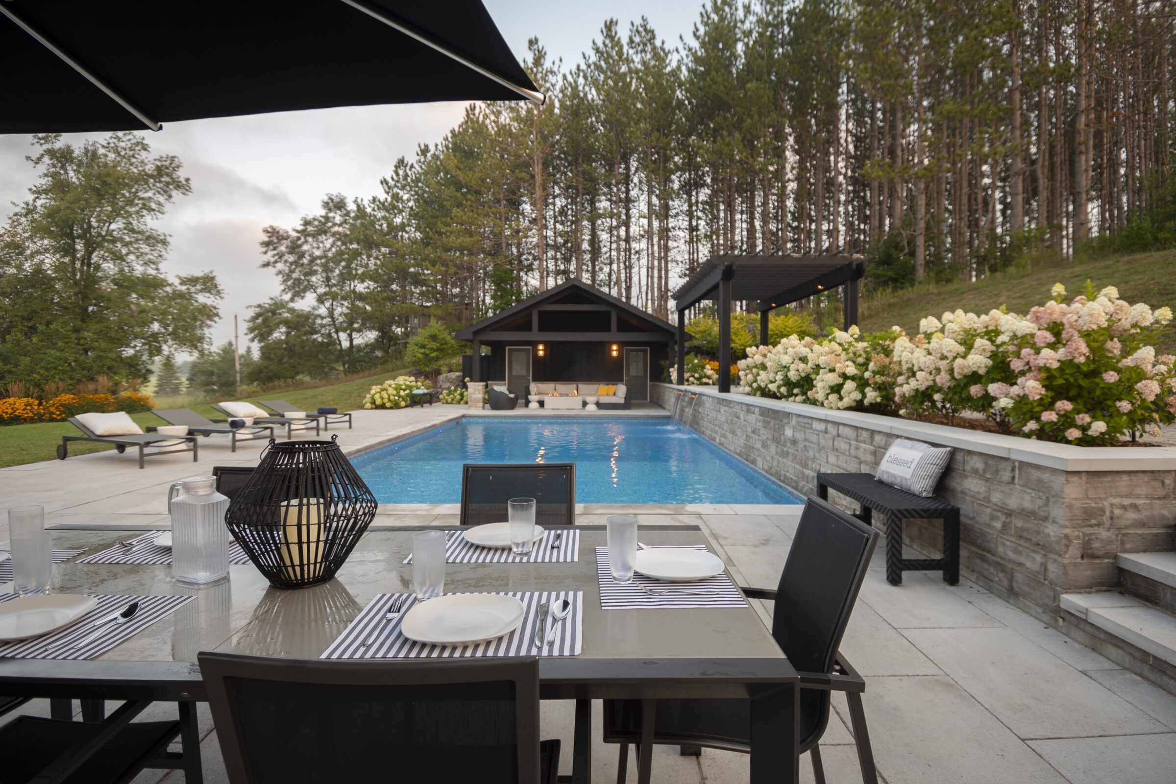 A tranquil backyard scene with a pool, elegant patio, dining table, and lush greenery; ideal for outdoor relaxation and gatherings.