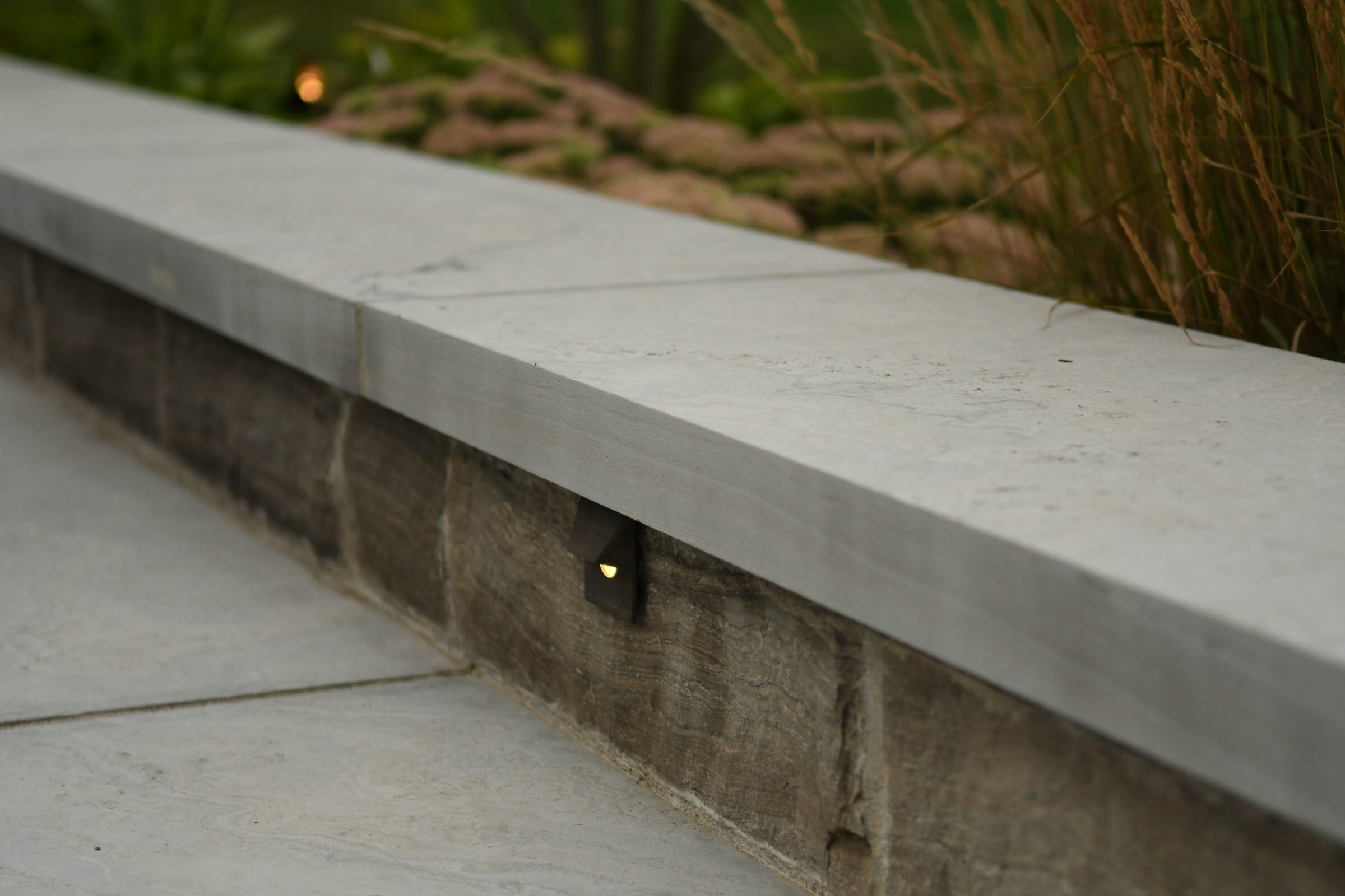 Stone ledge with embedded lighting, surrounded by greenery. Modern design complements the natural landscape, creating a serene outdoor ambiance.