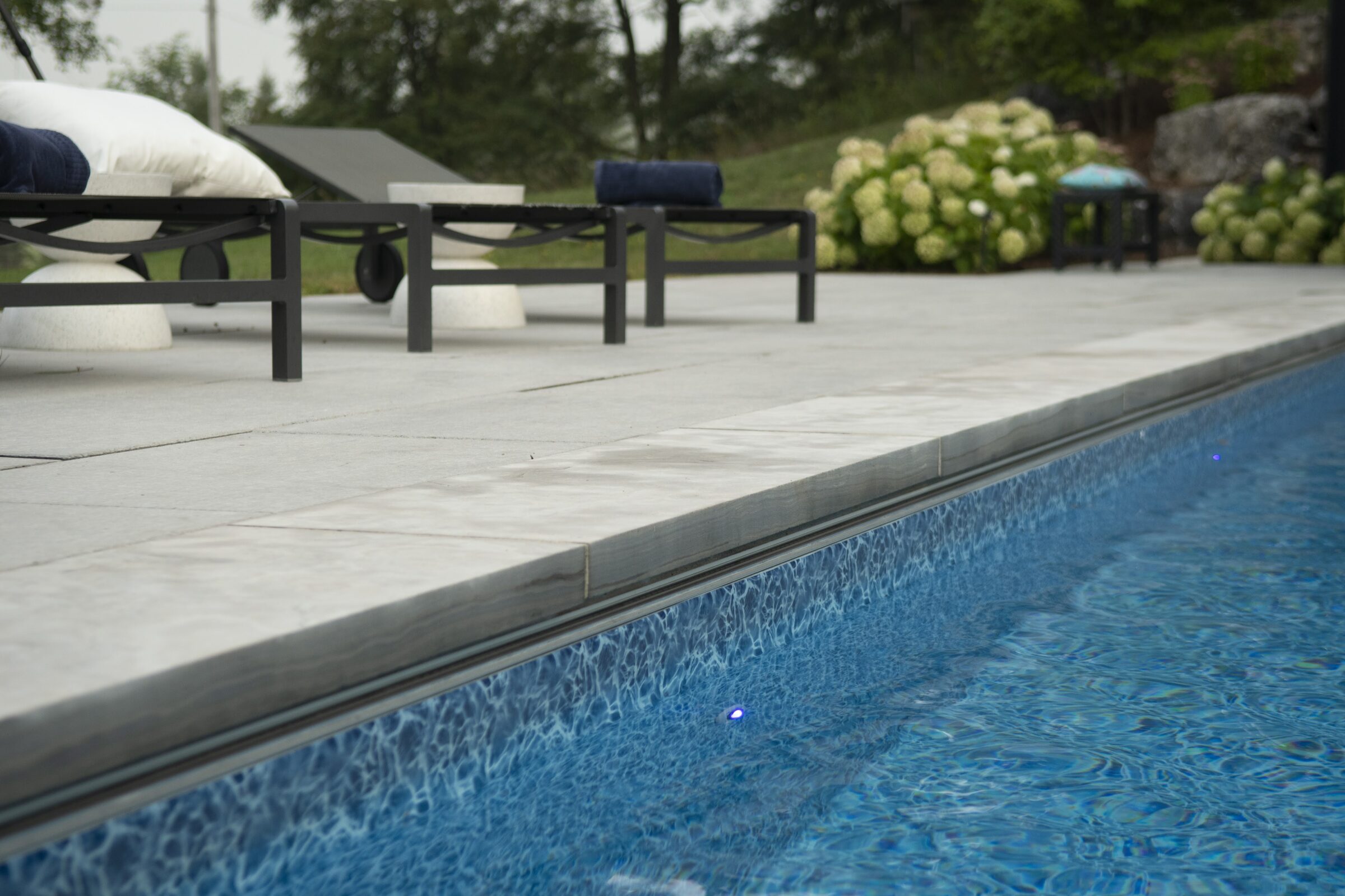 Poolside scene with clear blue water, lounge chairs, and lush greenery. Overcast sky provides a calm, peaceful atmosphere.