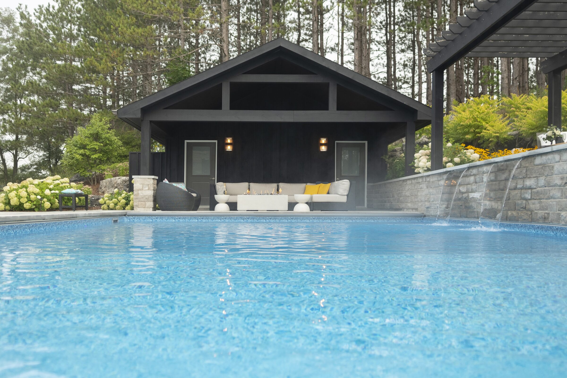 A tranquil poolside setting with a modern cabana, surrounded by lush greenery and cascading water features, offering a serene retreat.