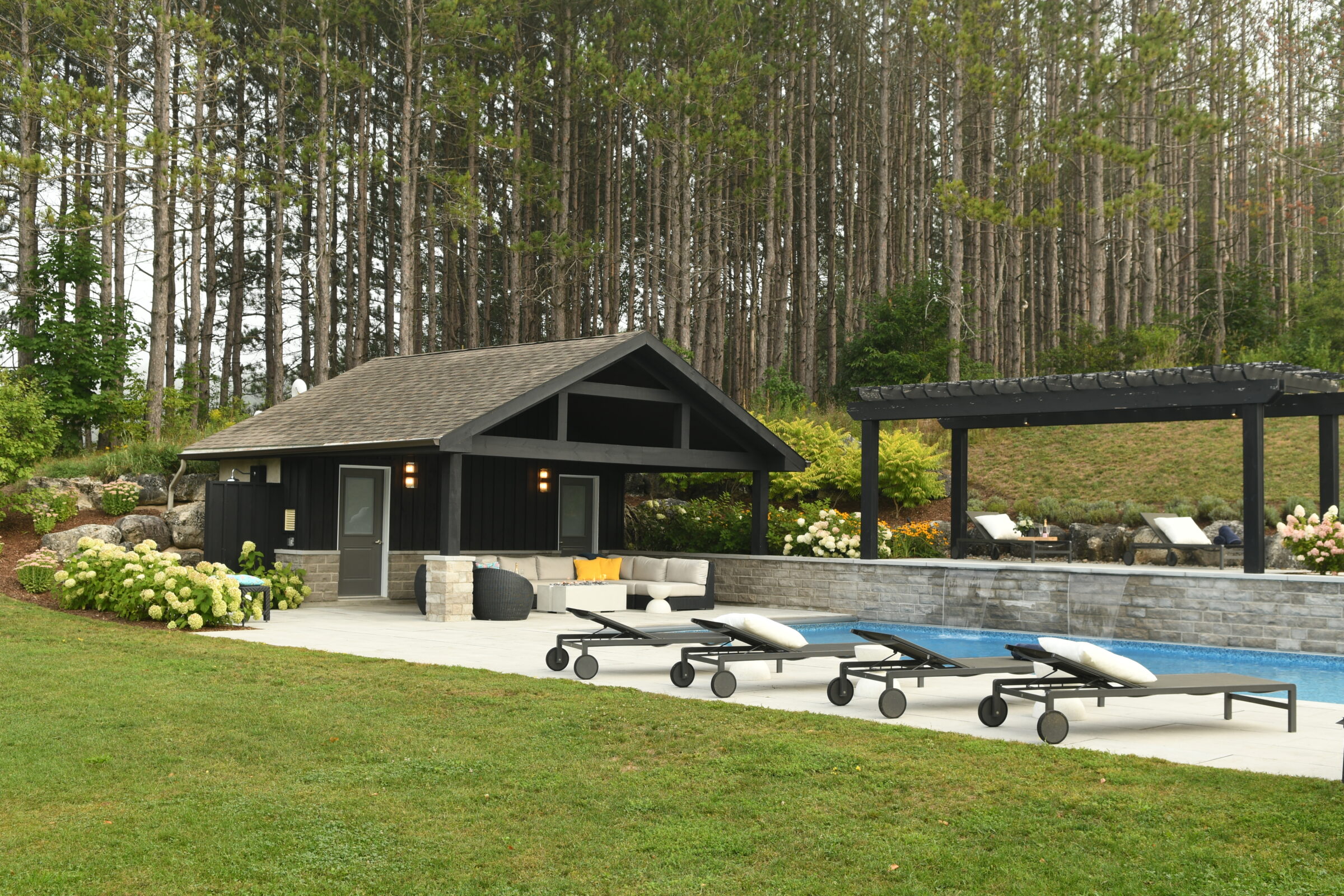 A serene poolside area with a small black pavilion, lounge chairs, and lush trees in the background, creating a peaceful retreat.
