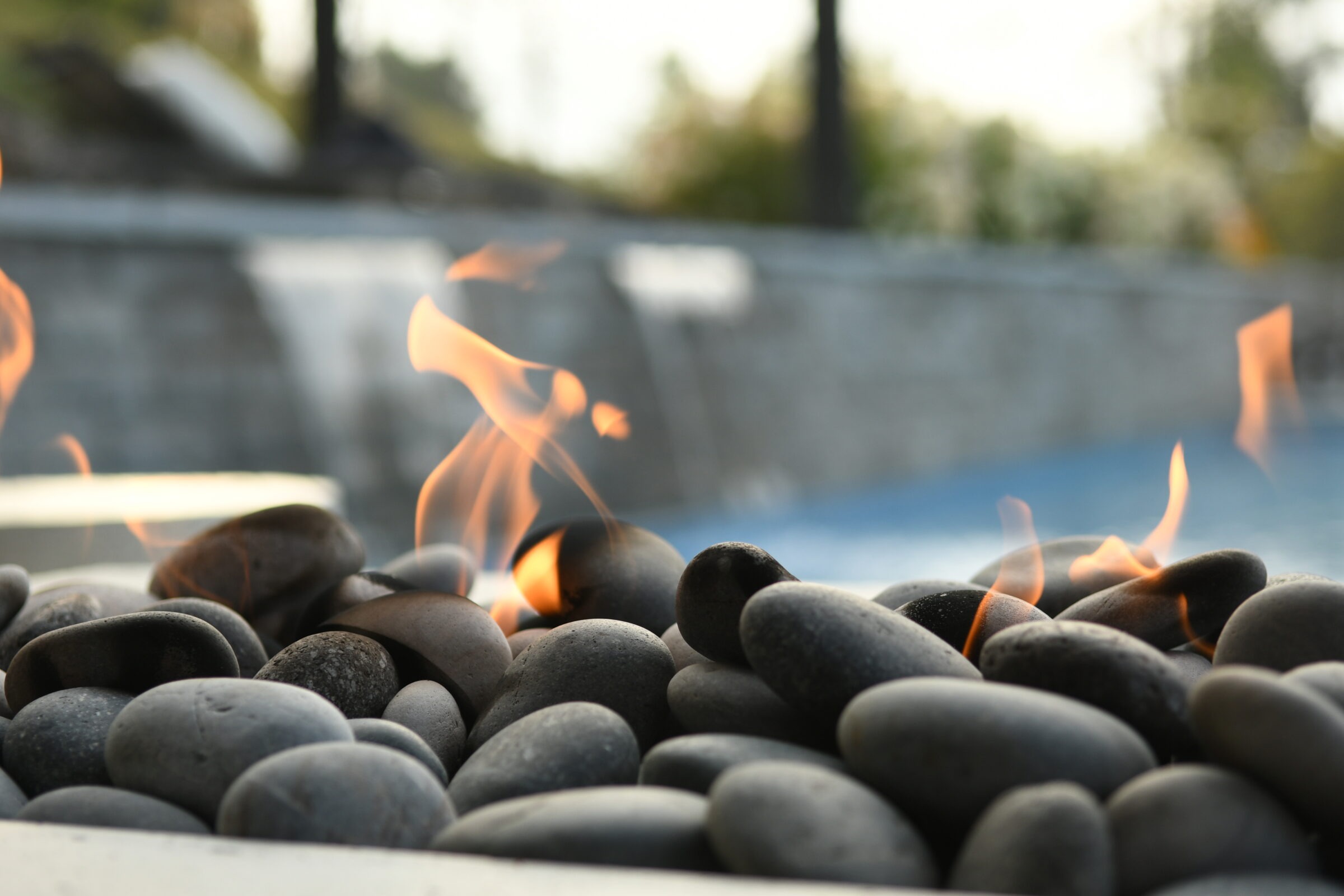 Smooth stones with small flames create a cozy ambiance in an outdoor setting, blurred background greenery enhances the tranquil atmosphere.