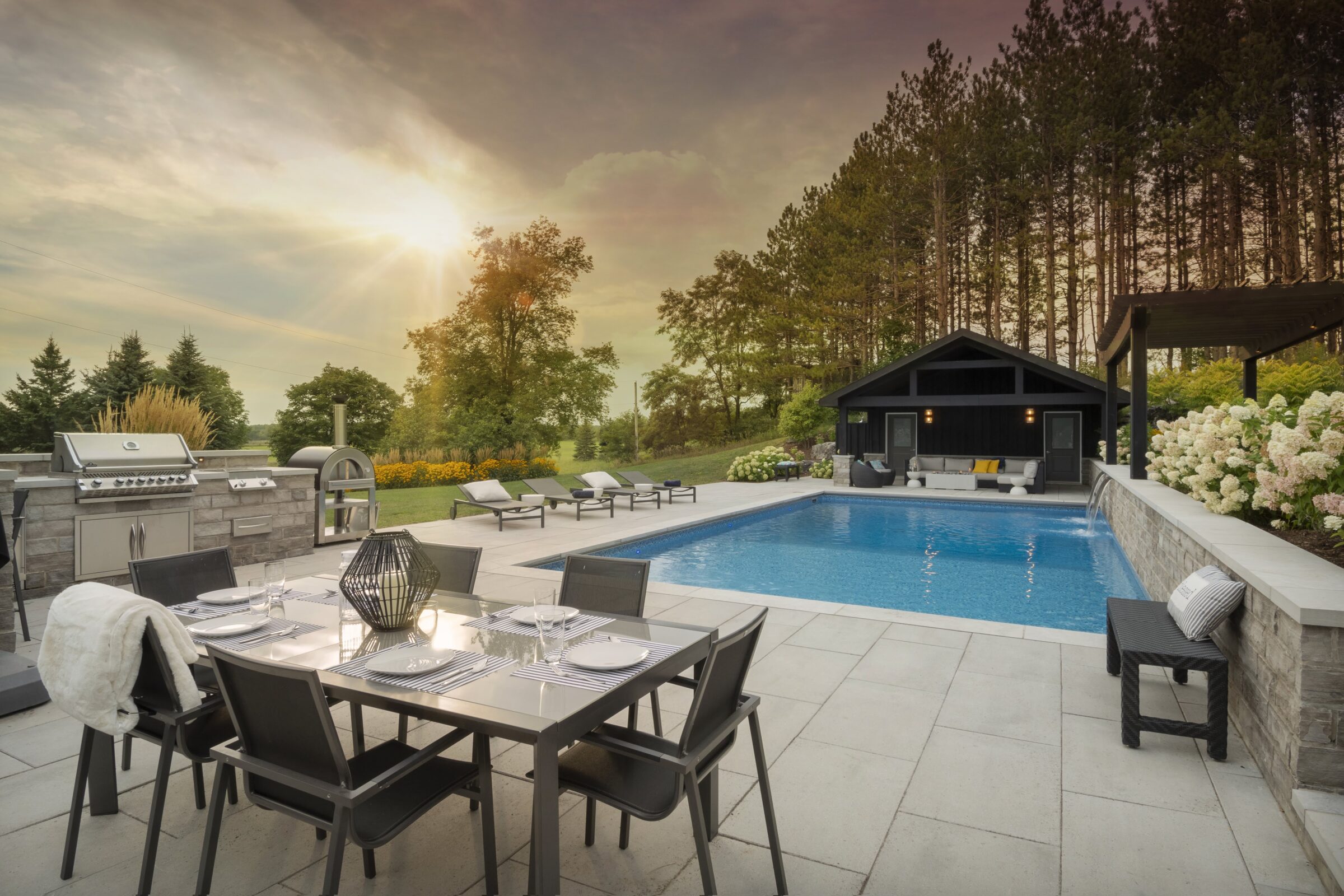 Elegant outdoor area featuring a pool, modern dining set, and sun loungers. A cozy pavilion with seating is surrounded by lush greenery.