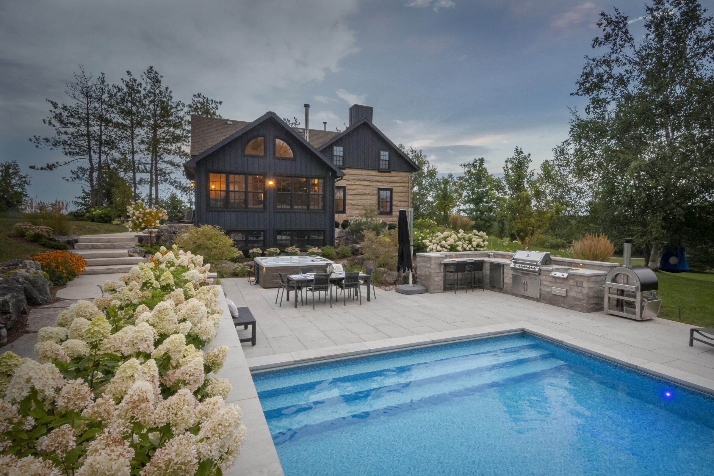 A beautiful backyard features a modern pool, patio, and landscaped garden, with an inviting house and outdoor kitchen under a cloudy sky.