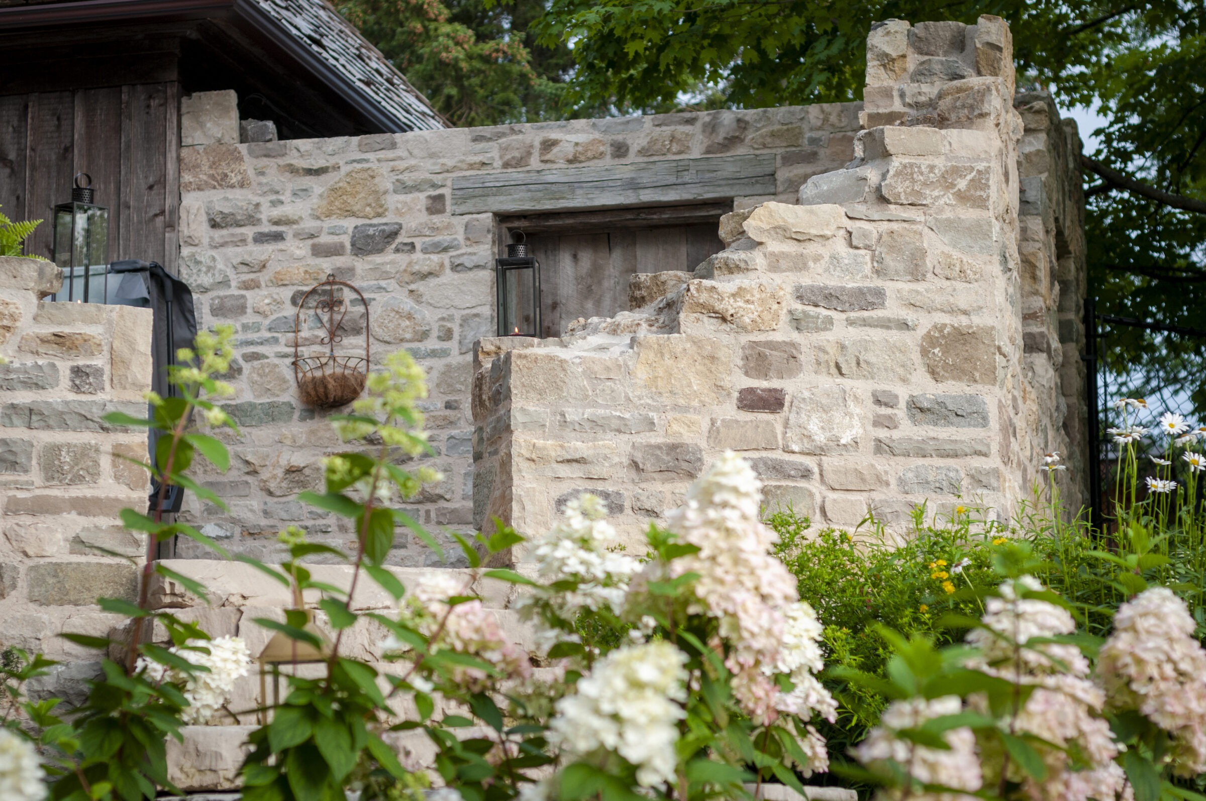 Stone building with rustic wooden door, surrounded by lush hydrangeas. The architectural style has a historic, charming appearance, complemented by a leafy backdrop.