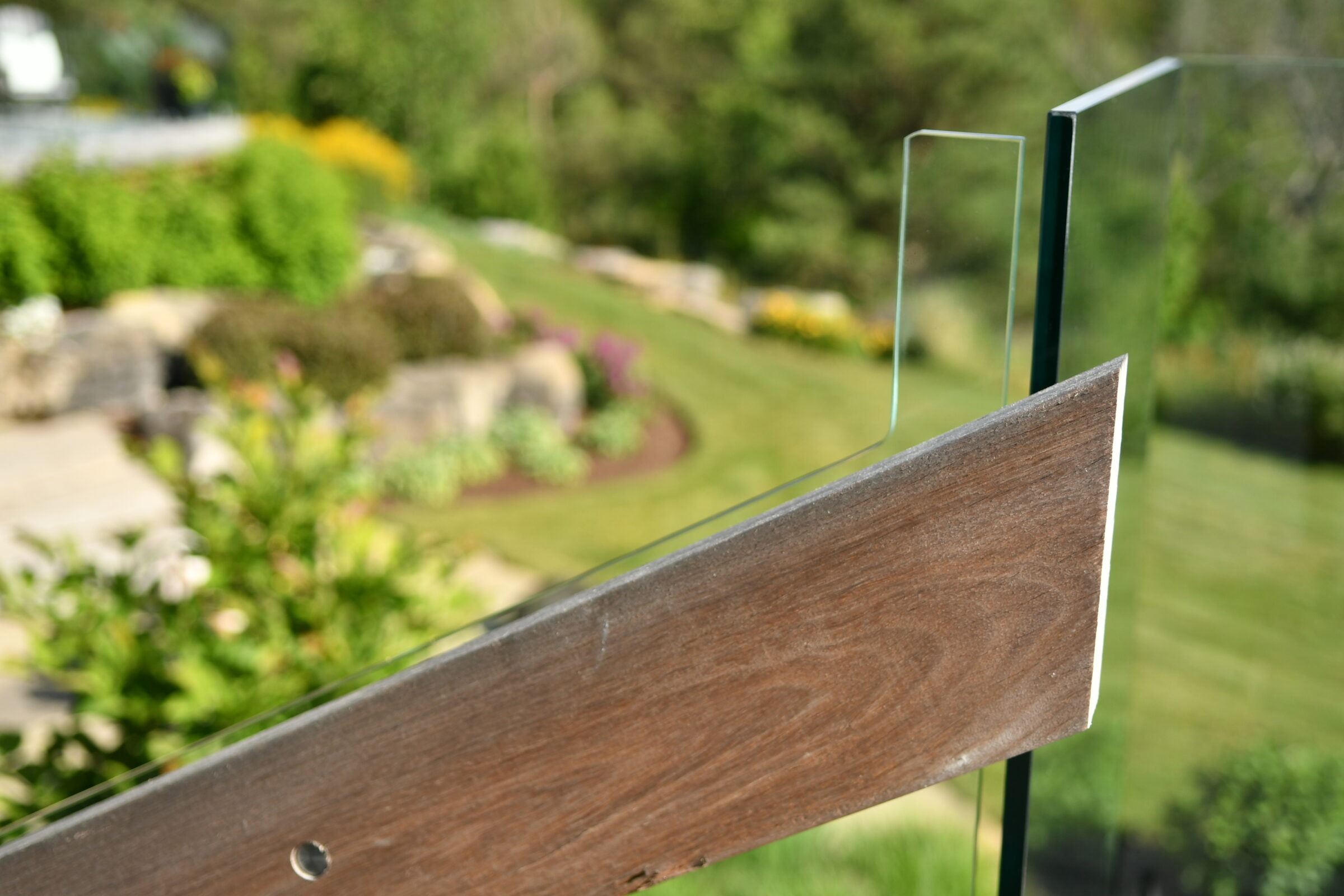 A landscaped garden with neatly trimmed grass, colorful flowerbeds, and a modern glass and wood railing in the foreground, creating a serene atmosphere.