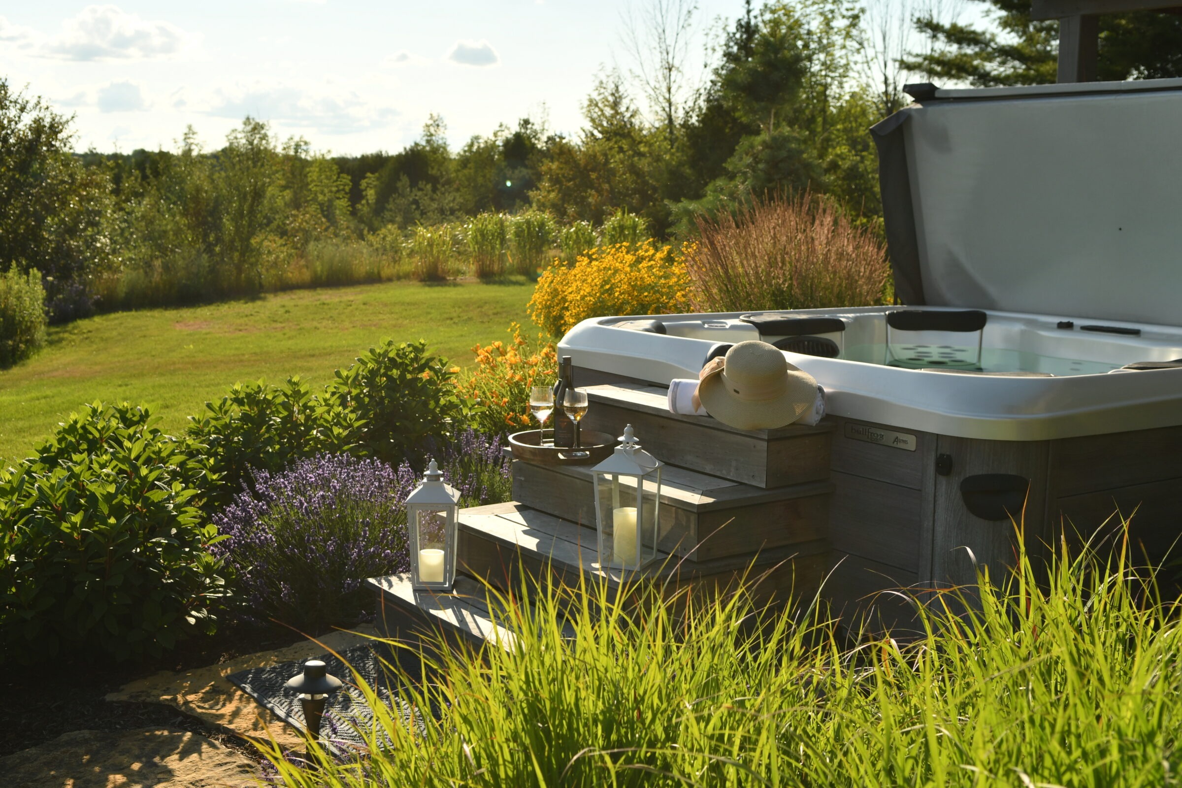 A tranquil garden scene with a hot tub, person relaxing with a sunhat, wine, and lanterns, surrounded by lush greenery and flowers.