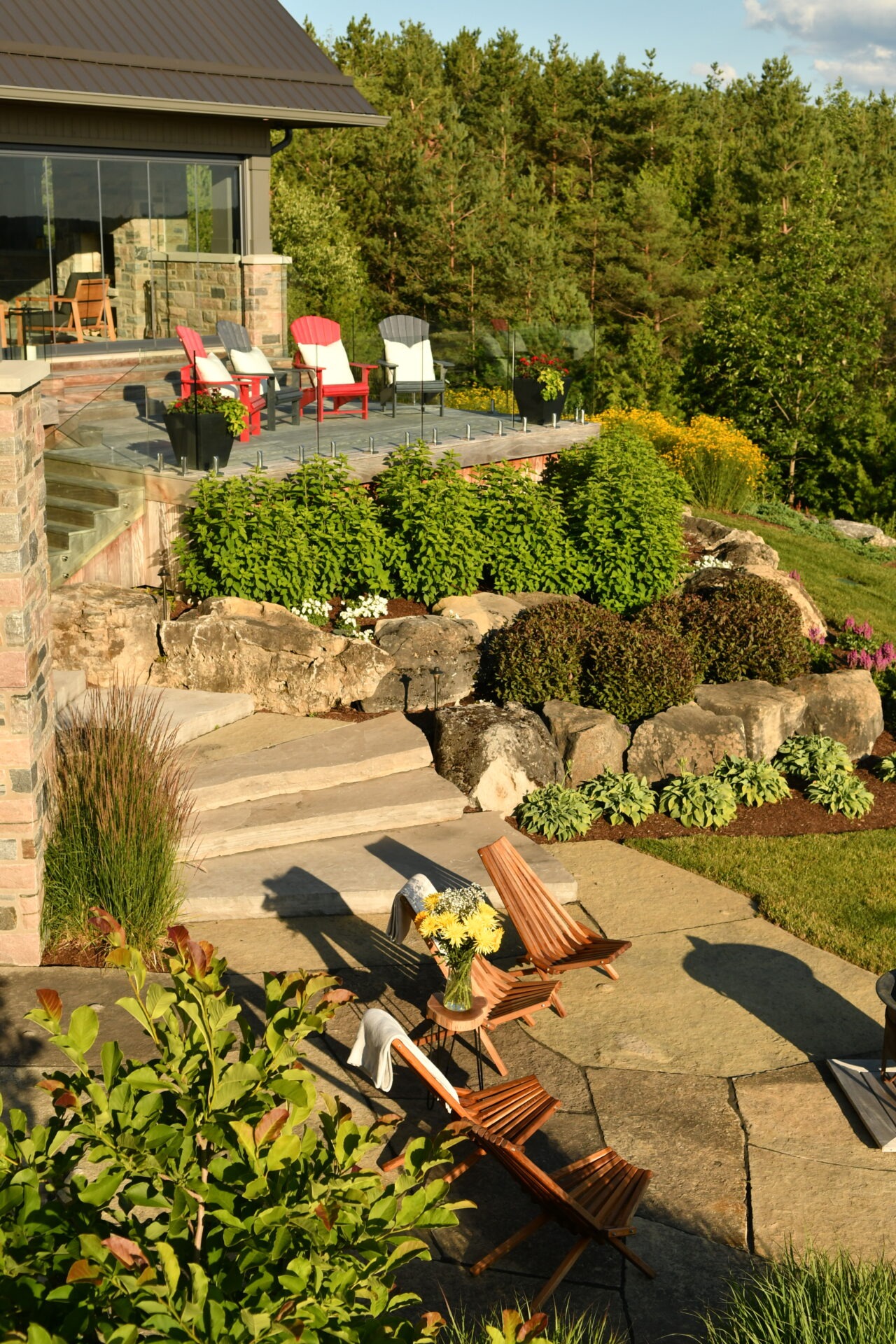 A scenic patio features colorful chairs, lush vegetation, and a forest backdrop, creating a relaxing outdoor space with abundant natural beauty.