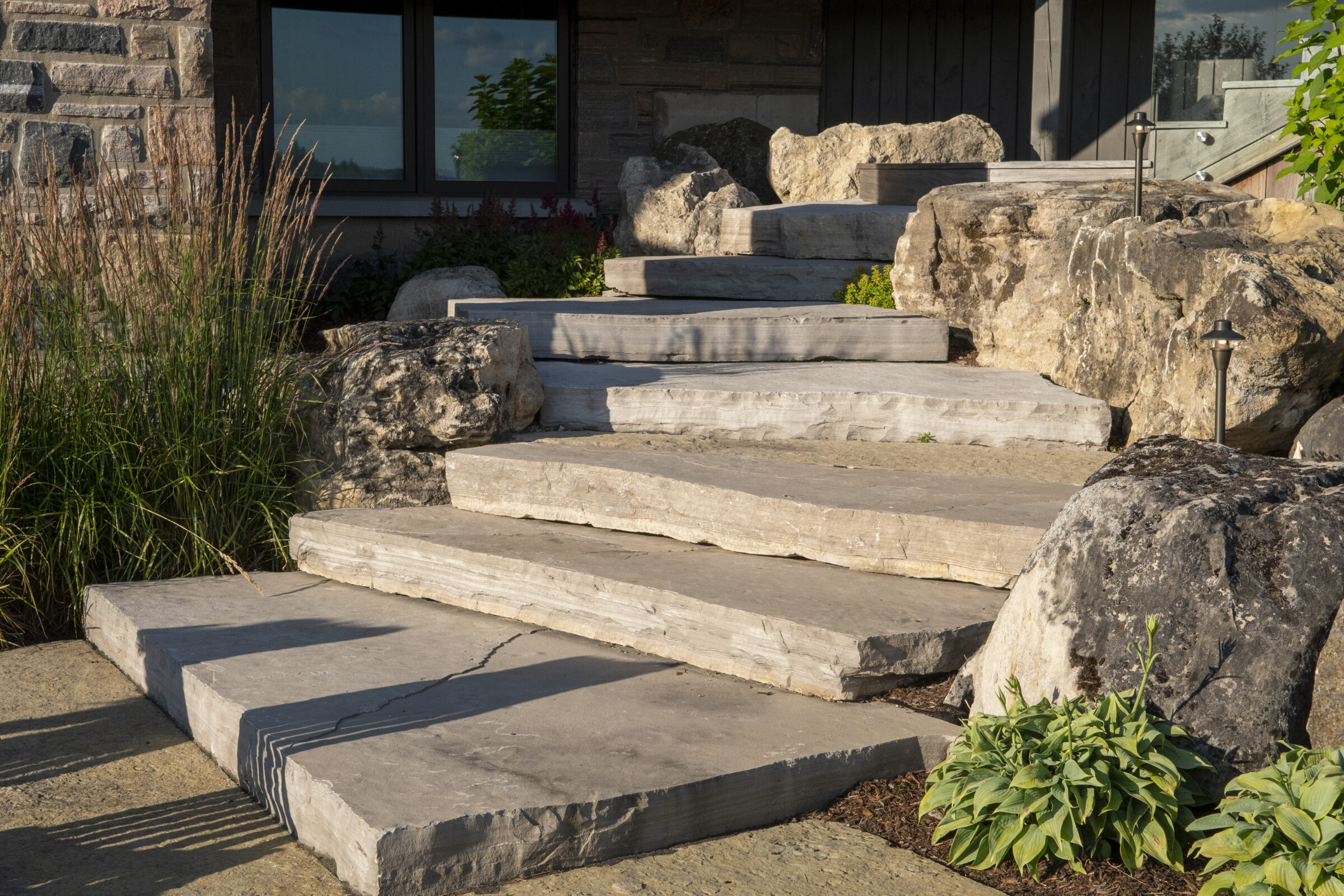 Stone steps leading to an entrance, bordered by decorative rocks and plants, with a modern brick exterior visible in the background.