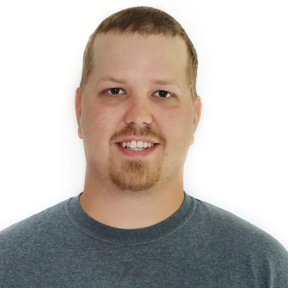 A person wearing a gray "Whispering Pines Landscaping" shirt smiles against a plain white background. No landmarks or historical buildings are visible.