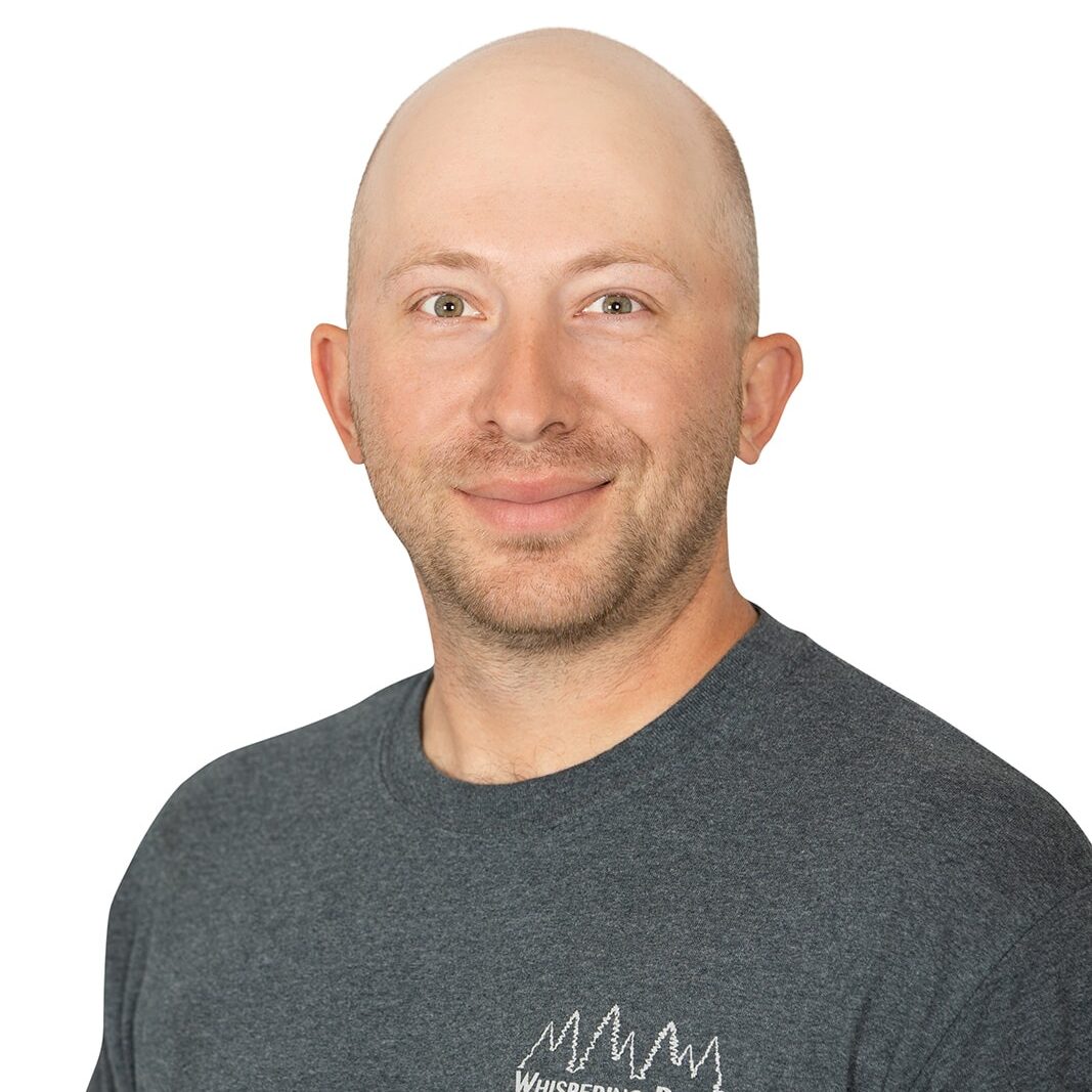 A person in a gray "Whispering Pines Landscaping" shirt smiles against a plain white background, suggesting a professional portrait or business advertisement.