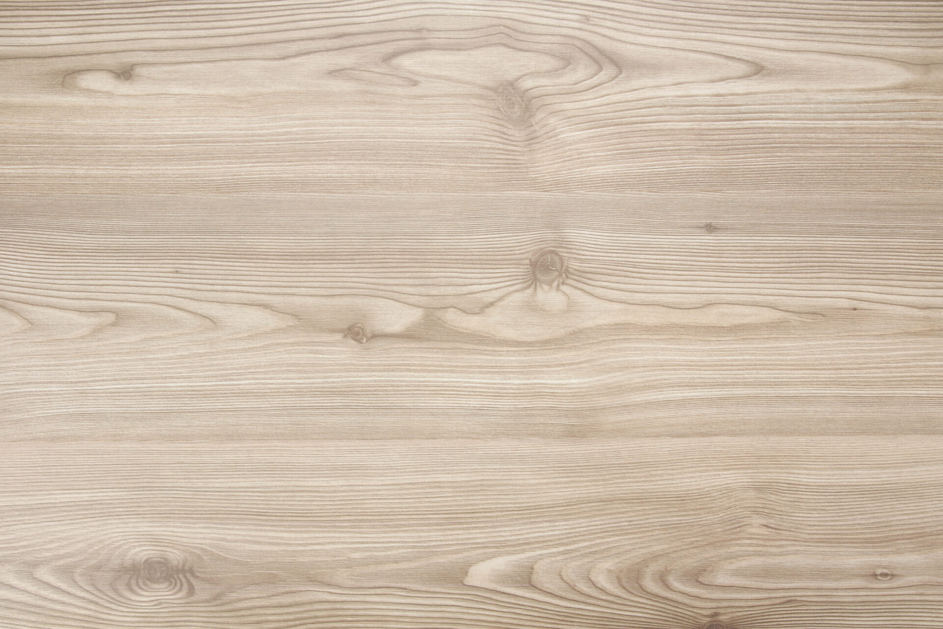 A close-up of light-colored wooden surface with natural grain patterns and knots, showcasing the detailed texture of the wood.