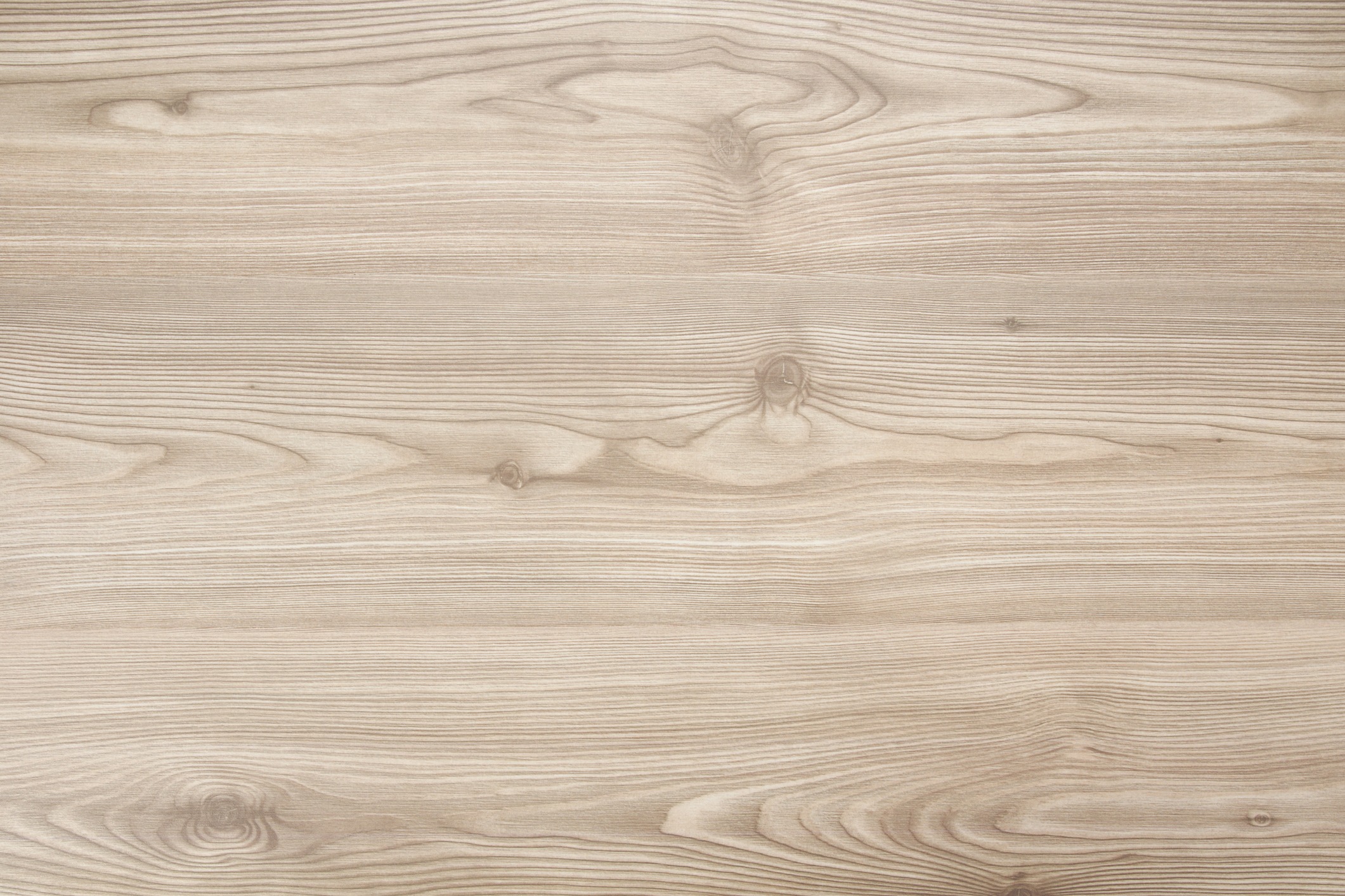 A close-up of light-colored wooden surface with natural grain patterns and knots, showcasing the detailed texture of the wood.