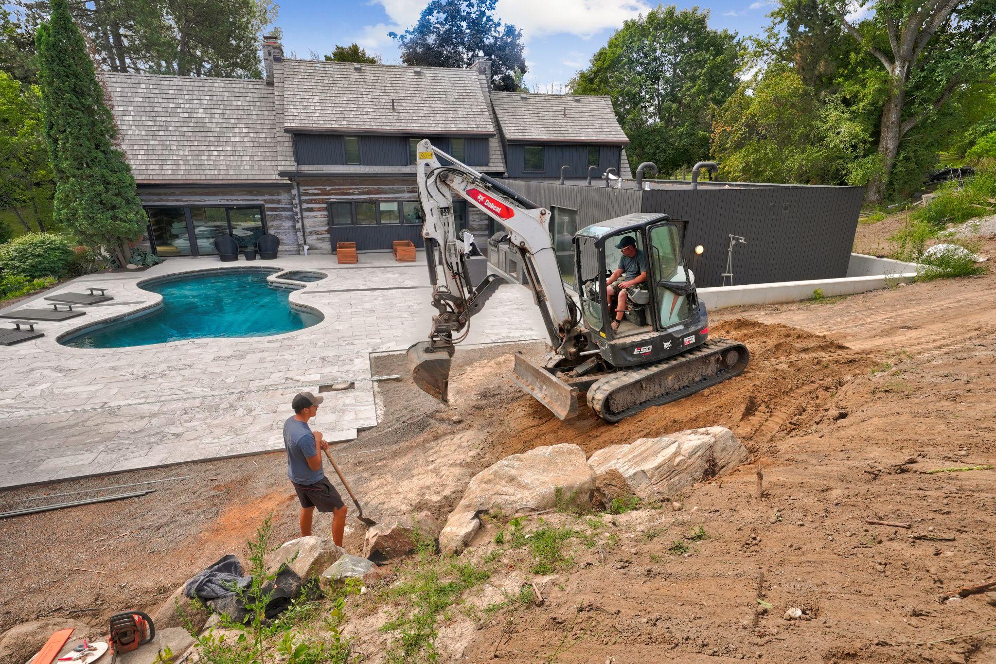 Excavator working near a backyard pool during patio construction.