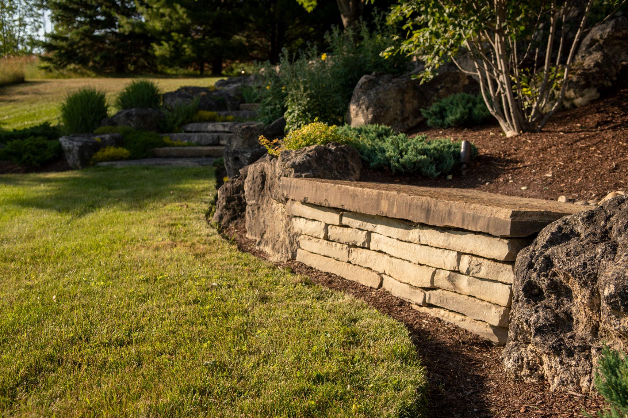 Natural stone retaining wall and steps along a landscaped residential hillside garden.