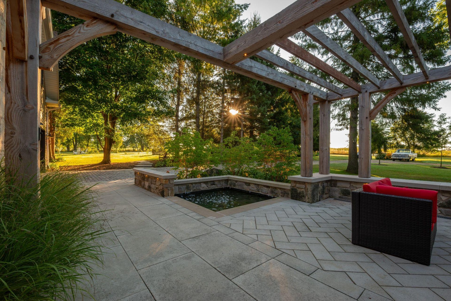 Pergola-covered interlocking stone patio with a reflecting pool at sunset.