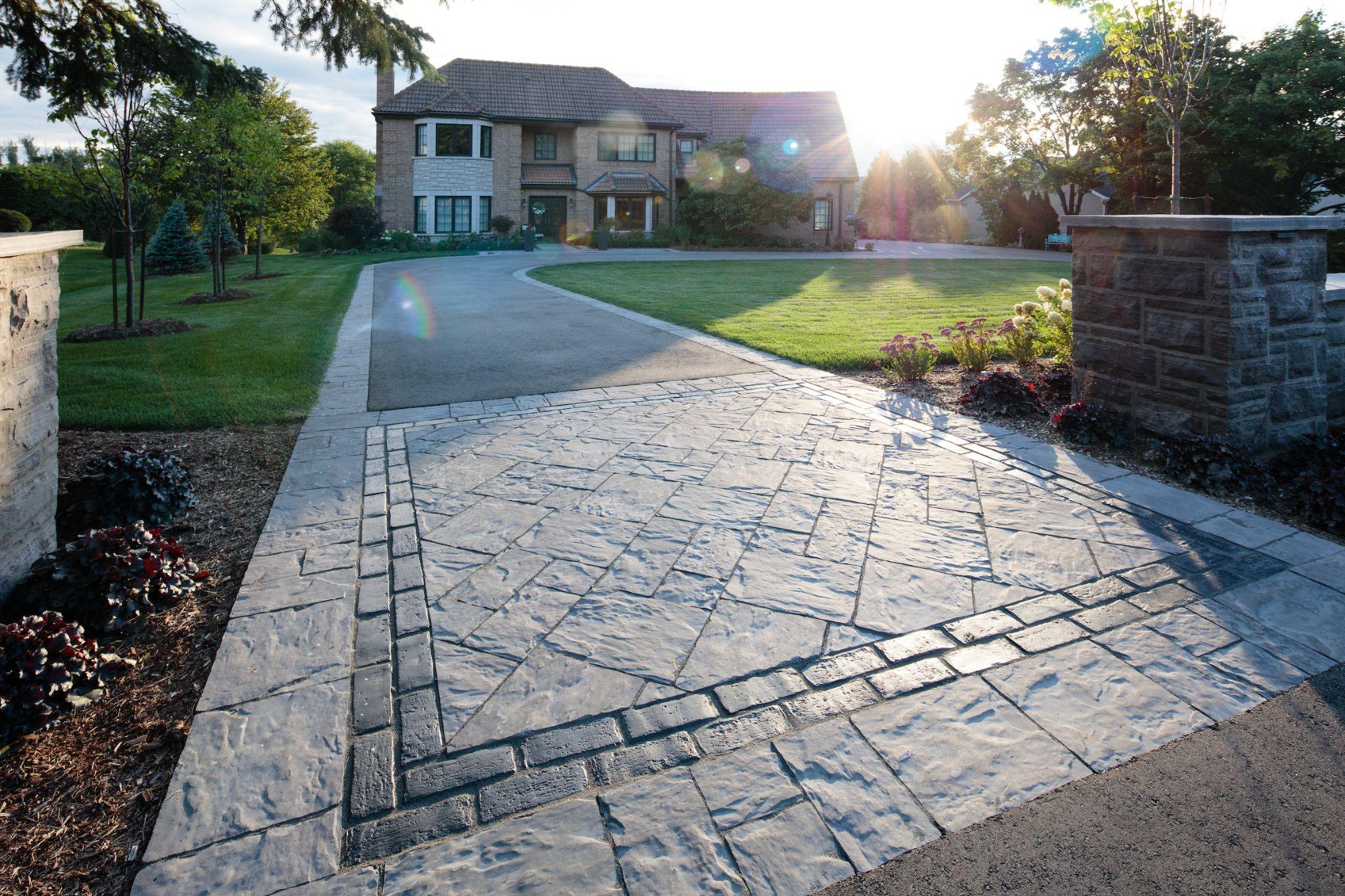 Combination stone and asphalt driveway leading to a brick estate home at sunrise.
