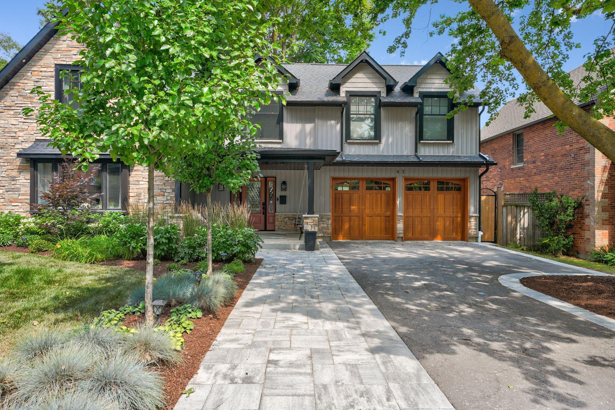 Two-story home with wooden garage doors with interlocking stone banding around an asphalt driveway